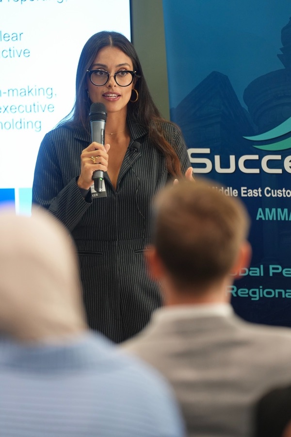 Ivy Forero holding a microphone, addressing a Customer Success conference audience